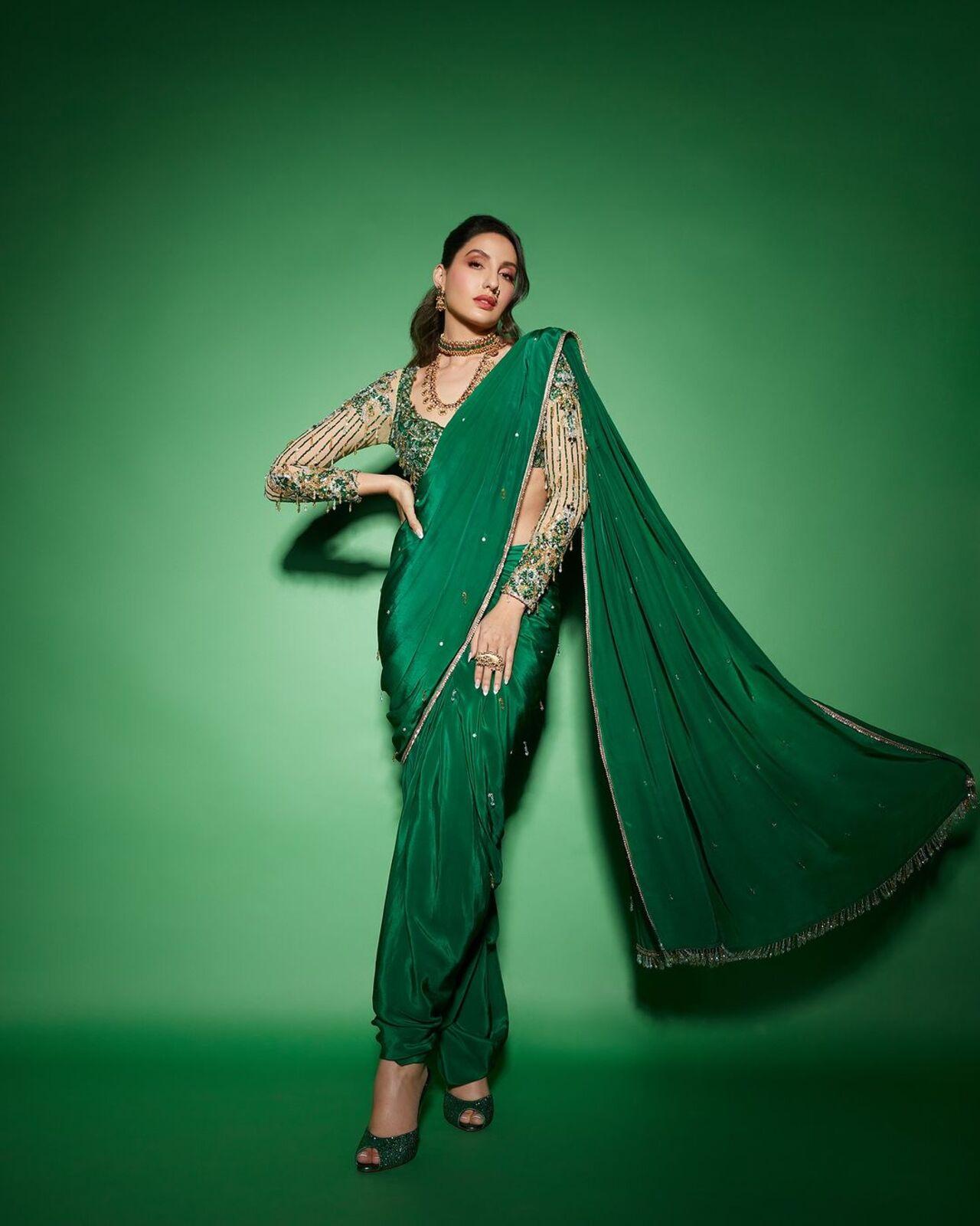 The beautiful Nora Fatehi is wearing a custom Nauvari emerald green color saree fabricated in silk. With a stone work border paired with a tulle blouse the ensemble showcases the richness of the embellished stones and sequins